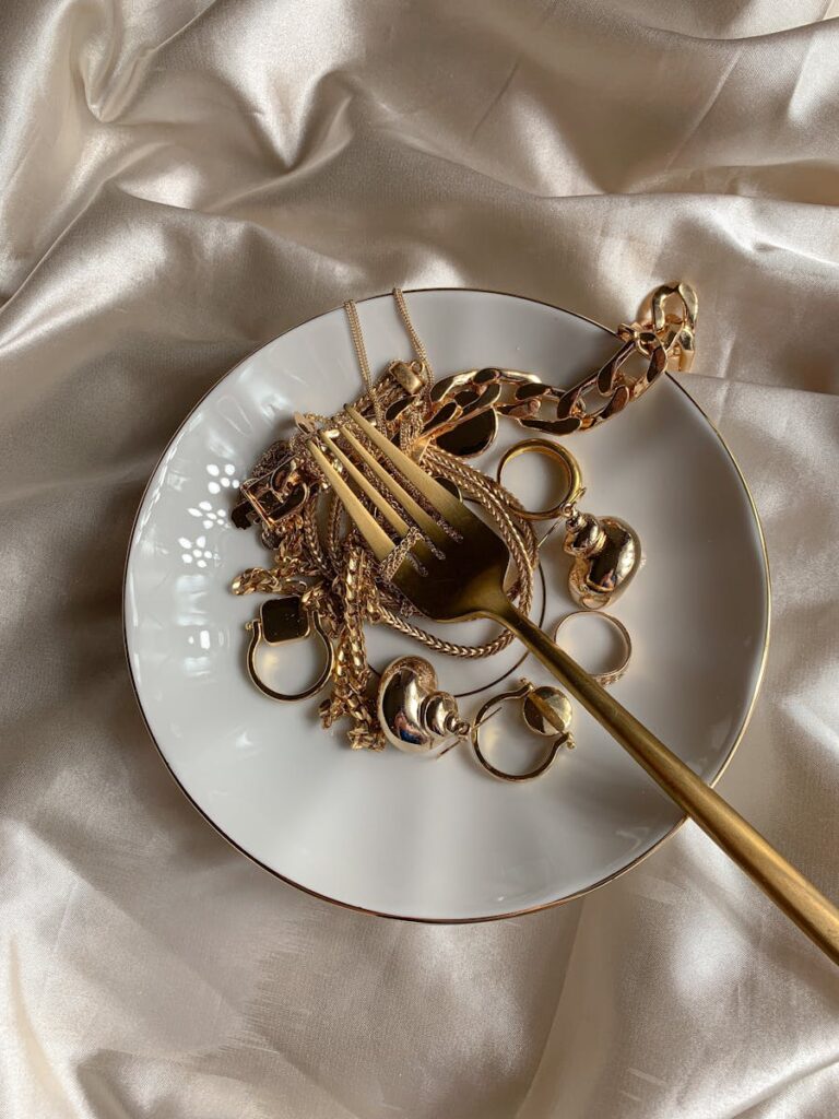 A close-up of luxurious gold jewelry on a ceramic plate with satin fabric backdrop.